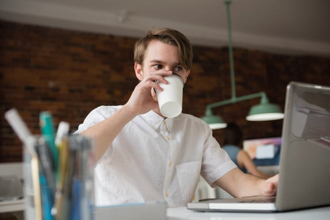 Male executive working on laptop while having coffee in office