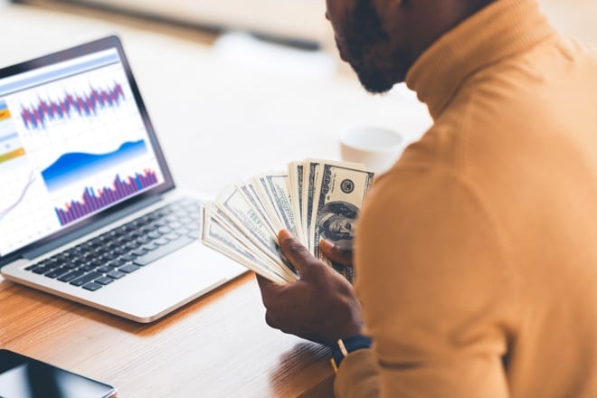 man holding cash looking at spreadsheet