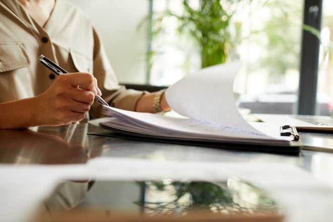 Close-up of manager sitting at the table holding pen and making notes in documents she doing paper work at office